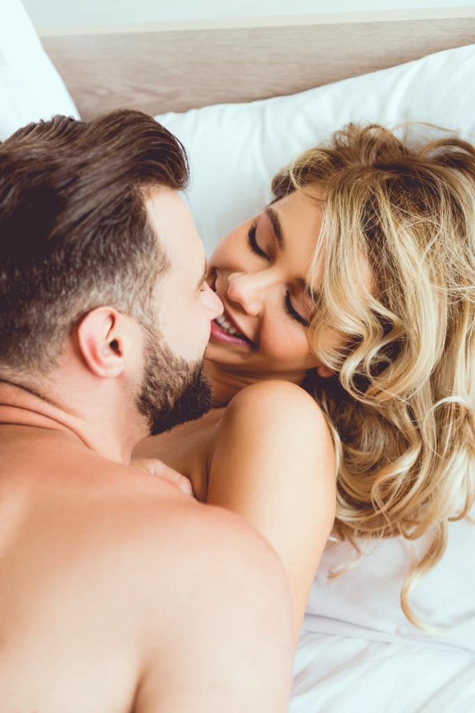 счастливая молодая пара обнимает и смотрит друг на друга, лежа в постели
 - Фото, изображение