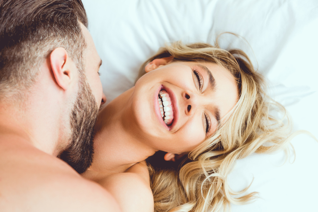 Ausgeschnittene Ansicht eines jungen Mannes, der lachende Freundin beißt, während sie im Bett liegt - Foto, Bild