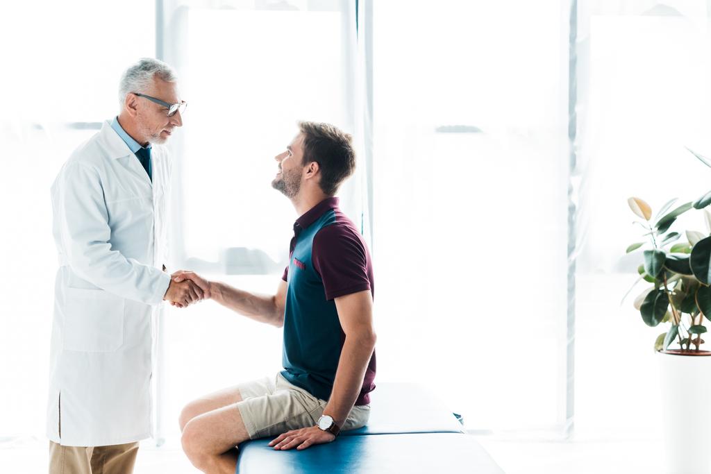 arts in glazen schudden handen met gelukkige man in kliniek  - Foto, afbeelding