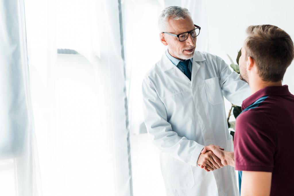 Glücklicher Arzt mit Brille schüttelt Mann in Klinik die Hand  - Foto, Bild