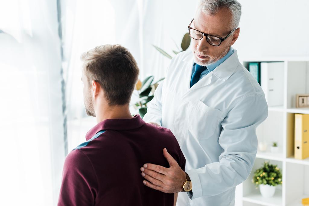 médico en gafas y bata blanca tocando la espalda del hombre en la clínica
  - Foto, imagen