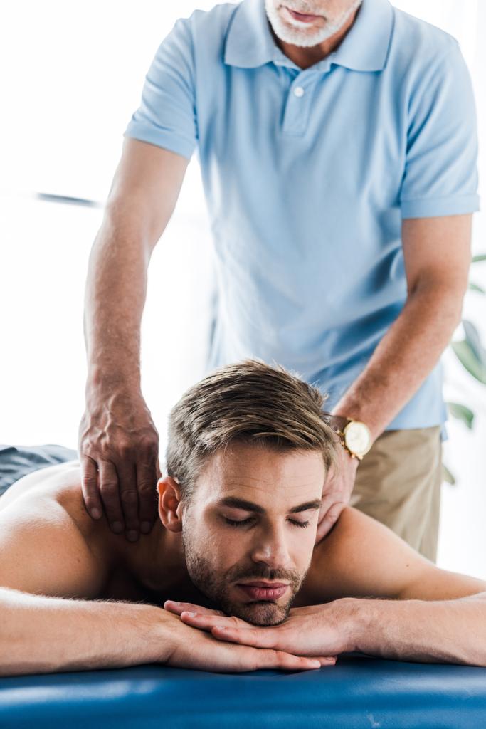 visão cortada de quiroprático barbudo fazendo massagem ao paciente com os olhos fechados
 - Foto, Imagem