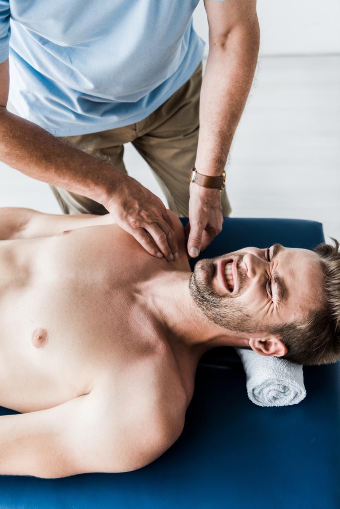 vista aérea del quiropráctico haciendo masaje al hombre con los ojos cerrados sufriendo dolor
  - Foto, Imagen