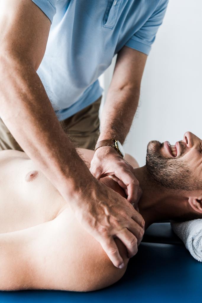 cropped view of chiropractor doing massage to man with closed eyes suffering pain  - Photo, Image