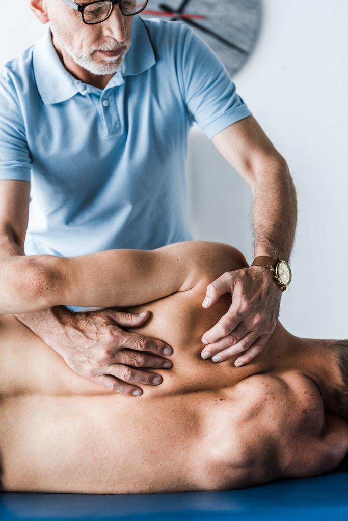 schöner Chiropraktiker berührt Rücken des Mannes auf Massagetisch  - Foto, Bild