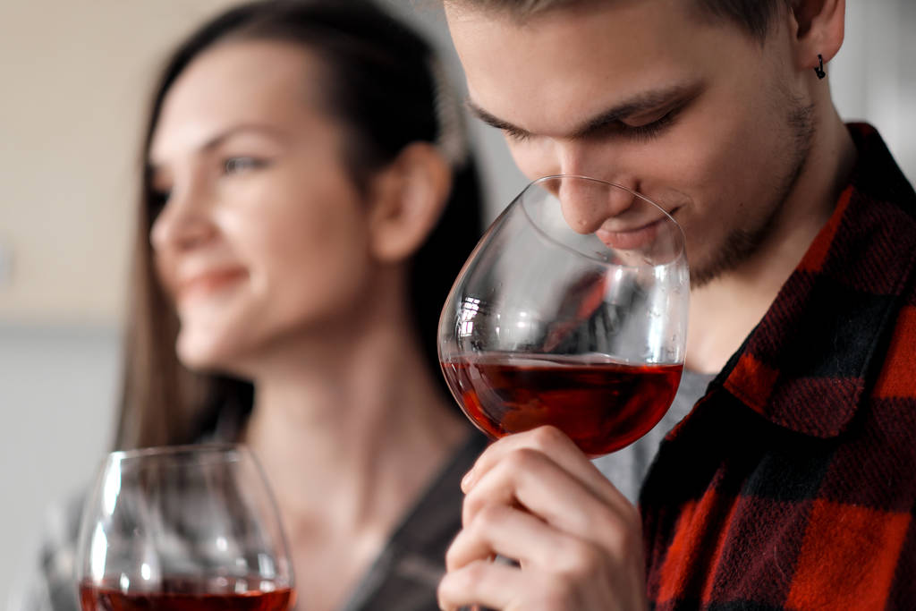 Красива молода пара в плетених сорочках на кухні готує їжу і п'є червоне вино з окулярів
. - Фото, зображення