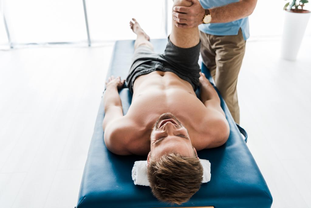 vista recortada del médico cerca del paciente acostado en la mesa de masaje y haciendo ejercicio en la clínica
  - Foto, imagen