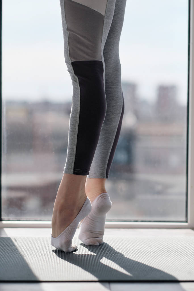 Close-up van vrouwelijke benen in sportkleding en sokken. Training van dansmoves en stretching op het balkon tegen het raam. - Foto, afbeelding
