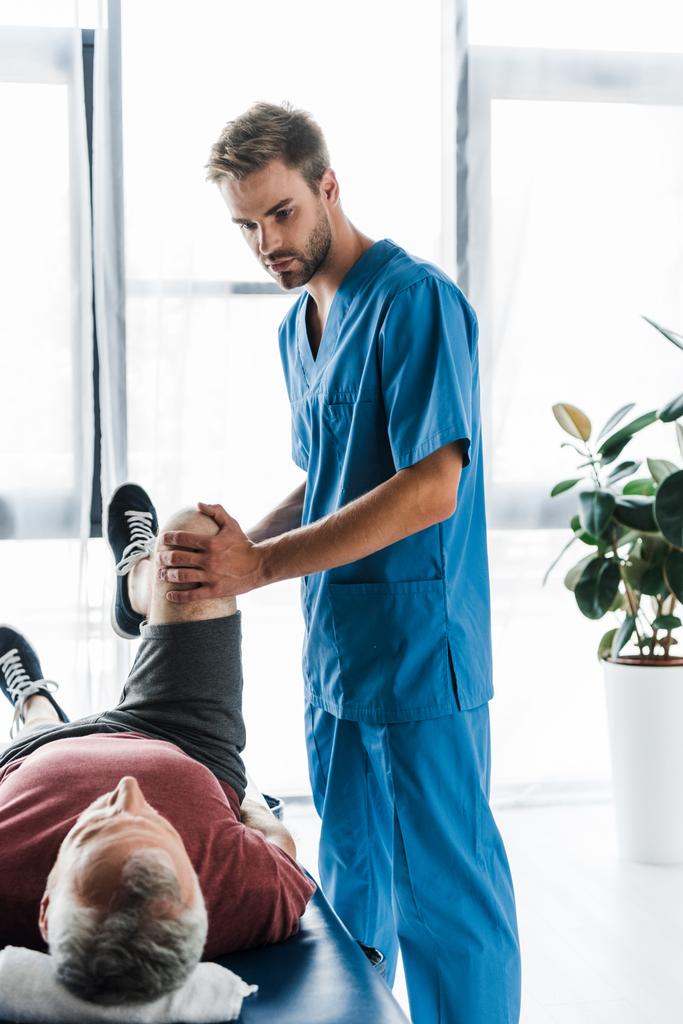 красивий лікар торкається ноги зрілого пацієнта вправи на масажному столі
  - Фото, зображення