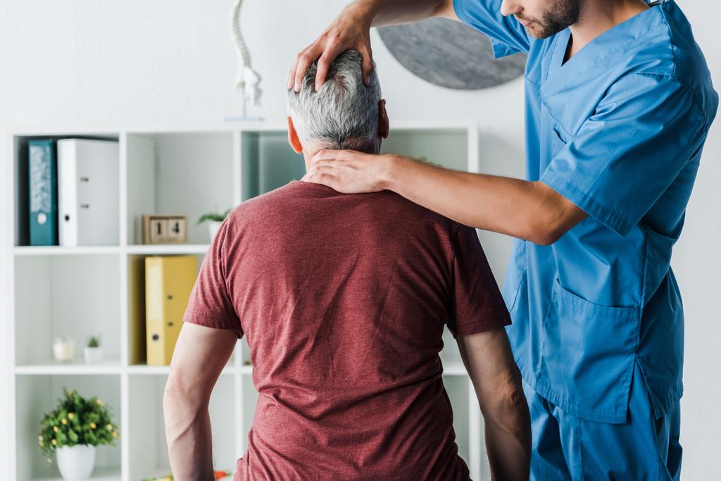 ostříhané zobrazení vousatého lékaře dotýkání se hlavy středně staršího pacienta na klinice - Fotografie, Obrázek