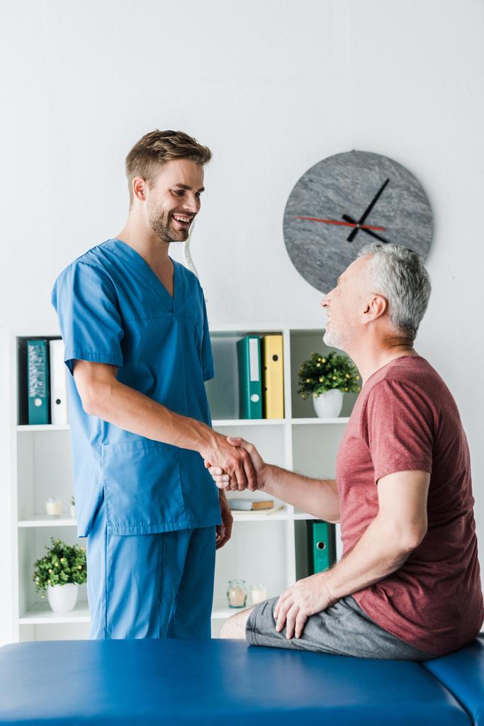 medico felice stringere la mano con allegro paziente maturo in clinica
  - Foto, immagini