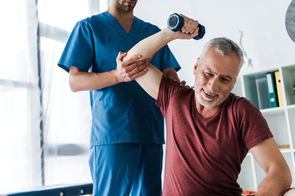 cropped view of doctor near mature man working out with dumbbell  - Photo, Image