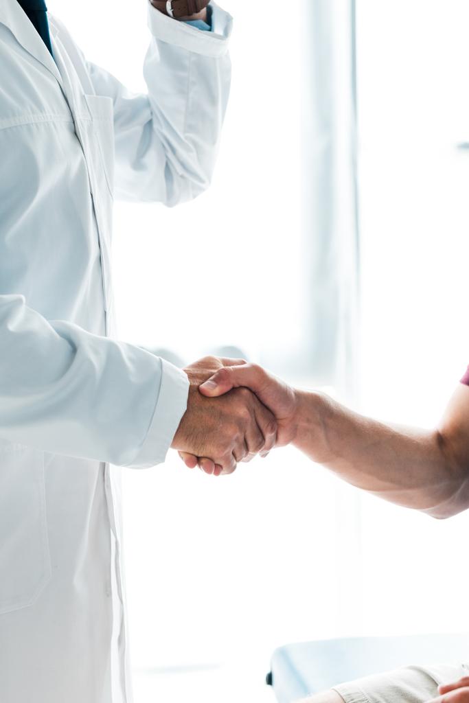 Ausgeschnittener Blick auf Arzt im weißen Kittel beim Händeschütteln mit Patient  - Foto, Bild