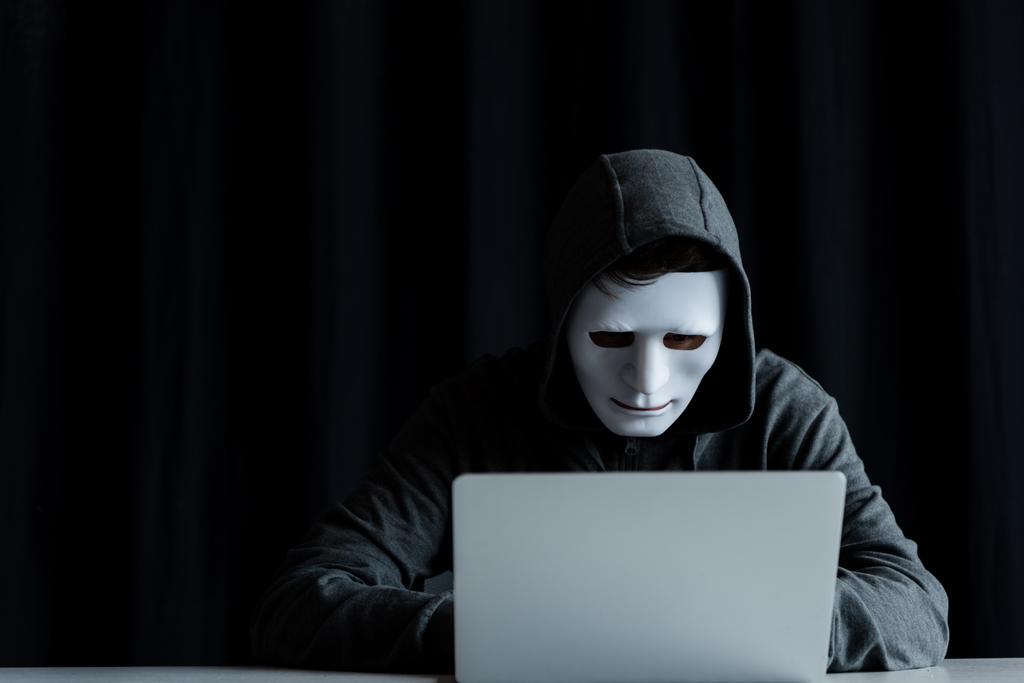 troll internet anonyme en masque tapant sur le clavier de l'ordinateur portable sur noir
 - Photo, image