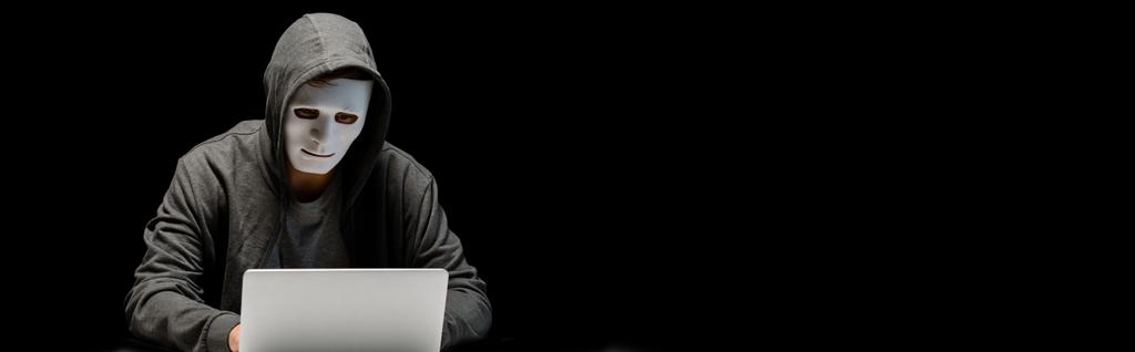 panoramiczny strzał anonimowego Internetu Troll w masce wpisując na klawiaturze laptopa na białym tle na czarno - Zdjęcie, obraz