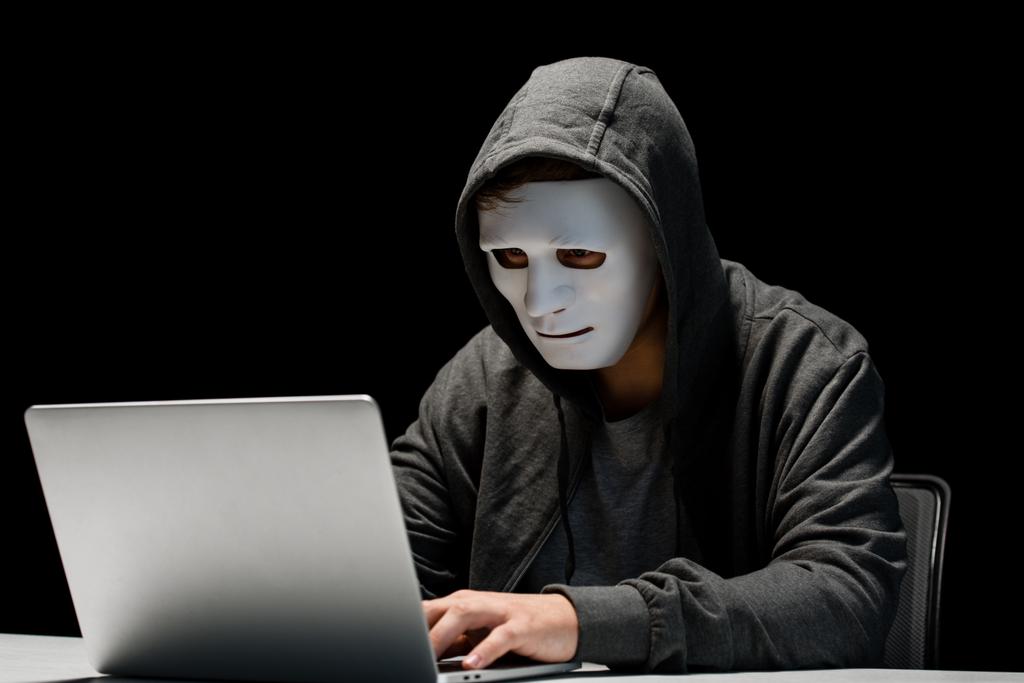 Ανώνυμος Διαδίκτυο τρολ σε μάσκα πληκτρολόγηση στο φορητό πληκτρολόγιο απομονώνεται σε μαύρο - Φωτογραφία, εικόνα