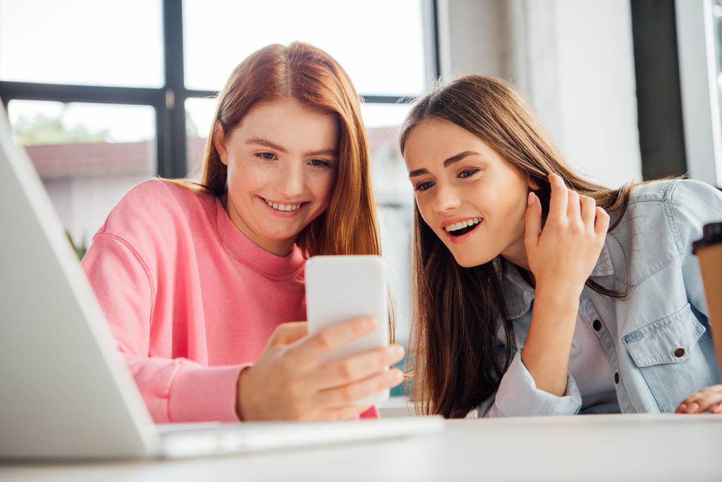 две взволнованные девушки улыбаются во время использования смартфона в школе
 - Фото, изображение