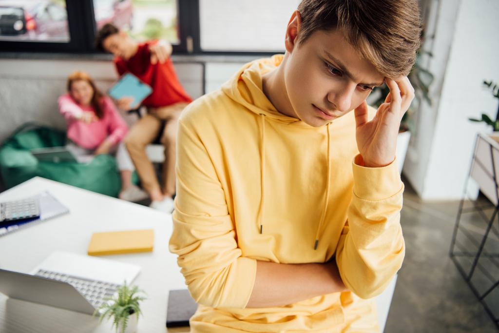 pensive boy in yellow hoodie and laughing classmates bullying him - Photo, Image