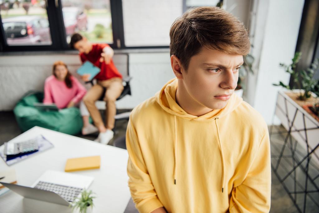 pensive boy in yellow hoodie and laughing classmates bullying him - Photo, Image