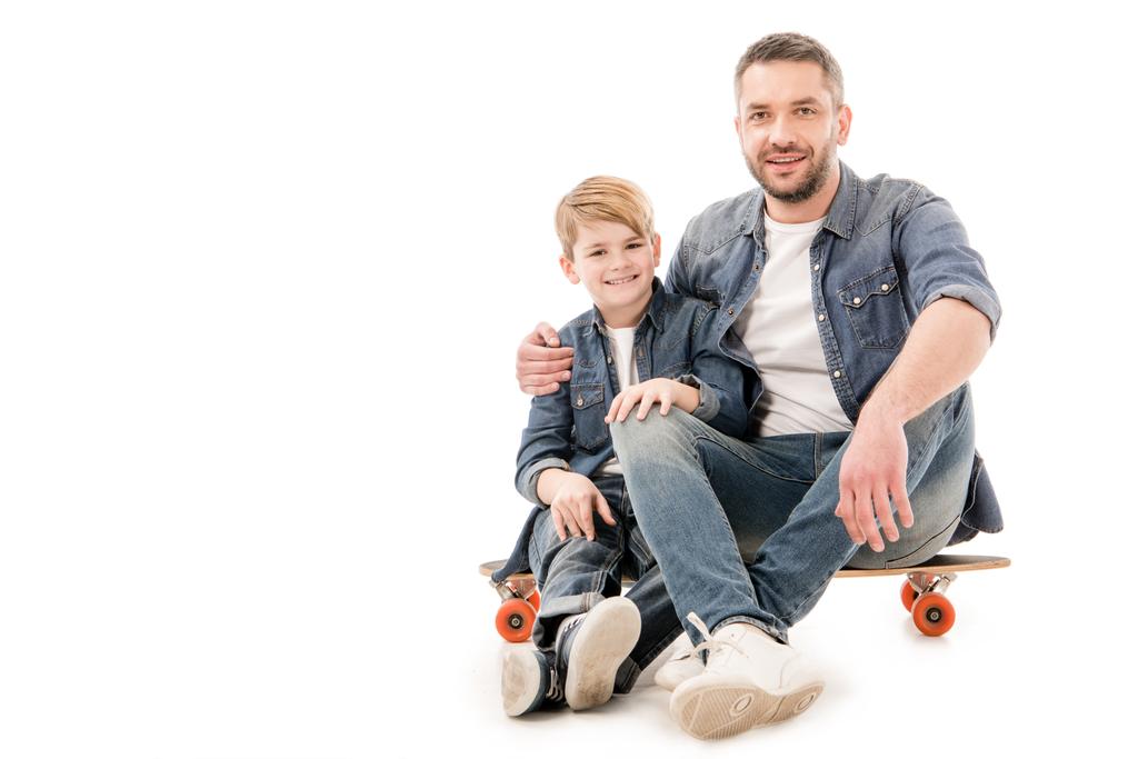 Sohn und Vater sitzen auf Skateboard und umarmen sich in Weiß - Foto, Bild