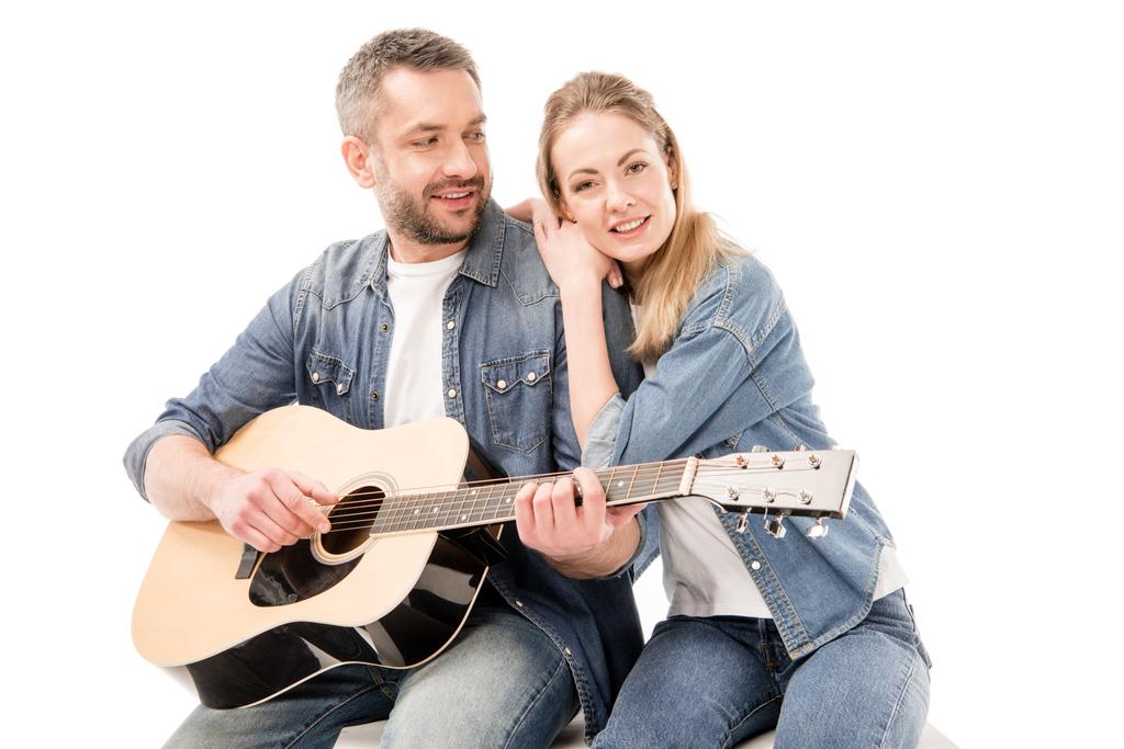 Улыбающийся мужчина в джинсах играет на акустической гитаре для жены, изолированной на белом
 - Фото, изображение