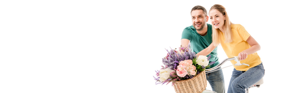 panoramic shot of happy couple with bike and basket of flowers isolated on white - Photo, Image