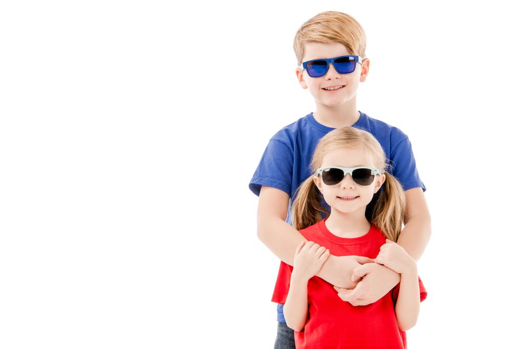 μπροστινή όψη της αδελφής και του αδελφού σε γυαλιά ηλίου που αγκαλιάζονται απομονωμένα σε λευκό - Φωτογραφία, εικόνα