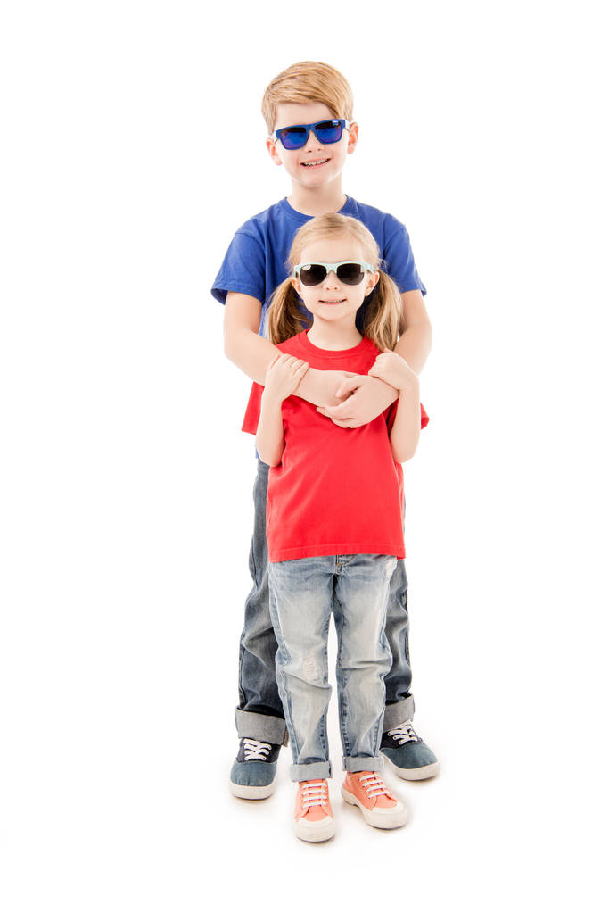 πλήρους μήκους θέα της αδελφής και του αδελφού σε γυαλιά ηλίου που αγκαλιάζονται απομονωμένα σε λευκό - Φωτογραφία, εικόνα
