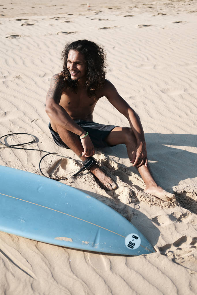 Mies Surfer istuu Surfboard hiekkarannalla
 - Valokuva, kuva