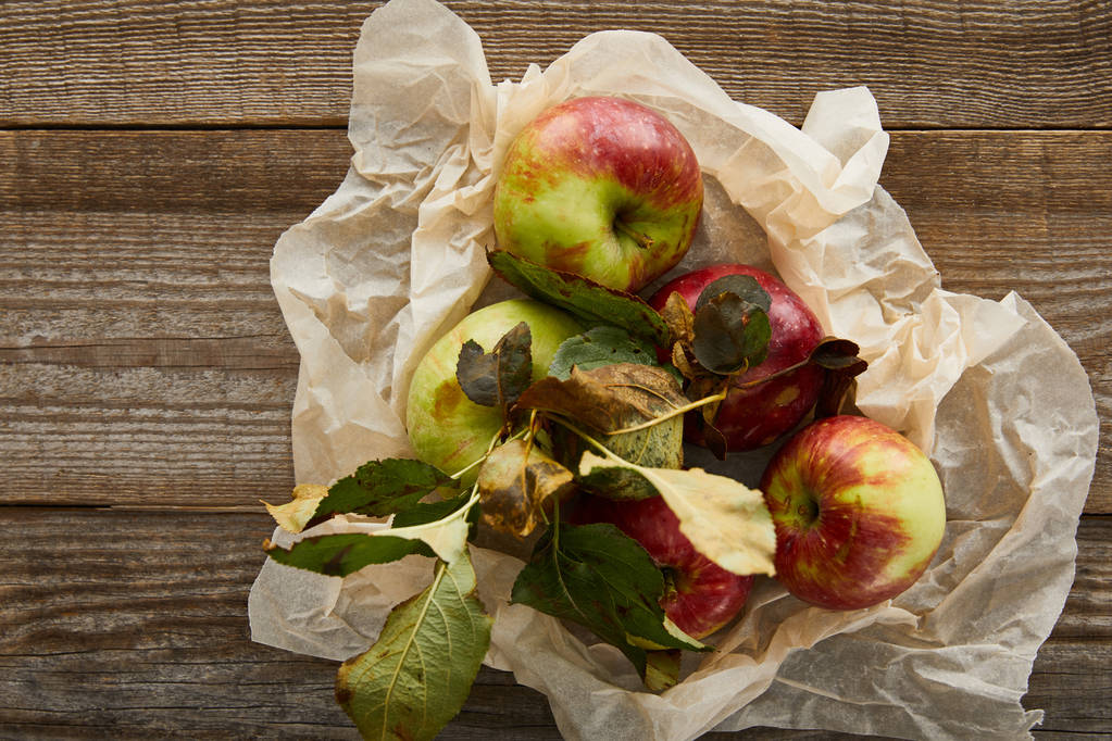 felsõ kilátás érett alma a levelek a gyűrt pergamen papír fa felületre - Fotó, kép