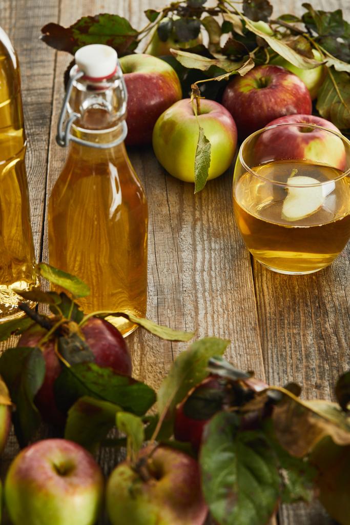 bottles and glass of fresh cider on wooden surface with ripe apples - Photo, Image