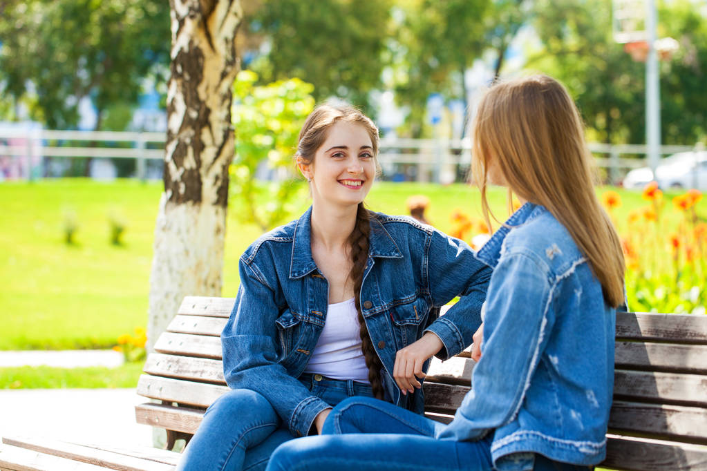 Two beautiful girlfriends are talking in a park sitting on a ben - Photo, Image