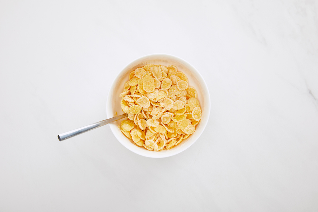 Draufsicht auf Schüssel Cornflakes mit Löffel auf weißem Marmor - Foto, Bild