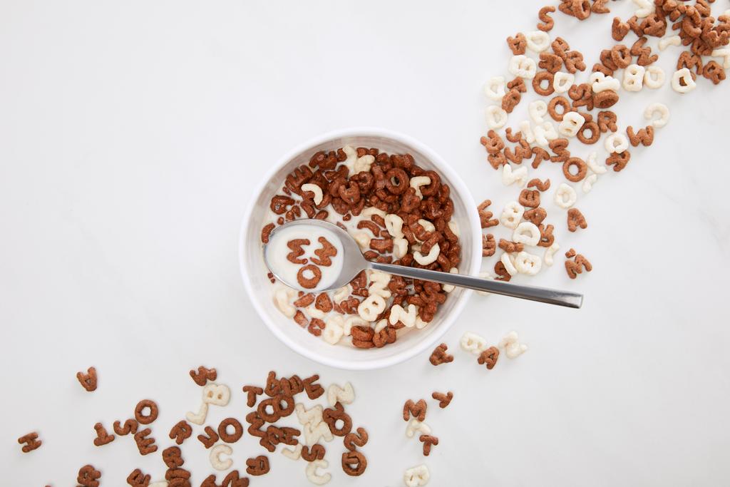 vista superior de la cuchara con la leche y el cereal wow inscripción en el tazón en la superficie de mármol
 - Foto, imagen