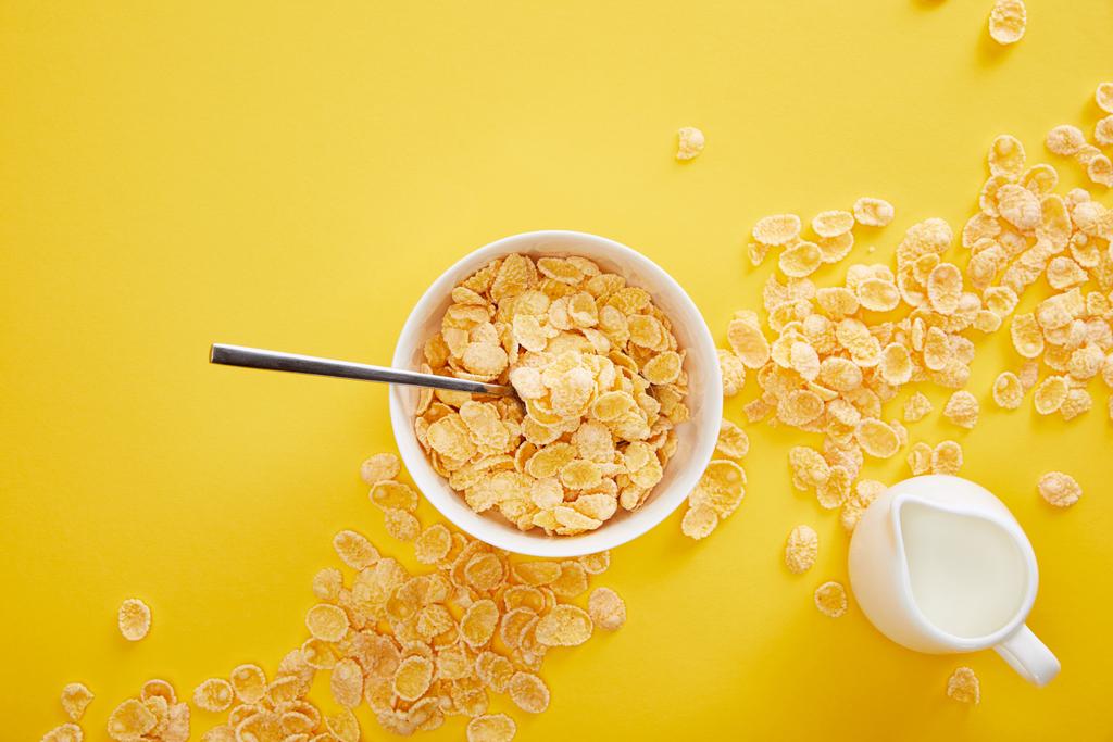 vue du dessus du bol avec des flocons de maïs près de morceaux épars et une cruche de lait isolé sur jaune
 - Photo, image