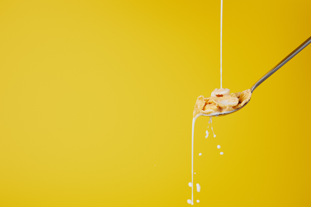 cuchara con copos de maíz y torrente de leche aislado en amarillo
 - Foto, Imagen