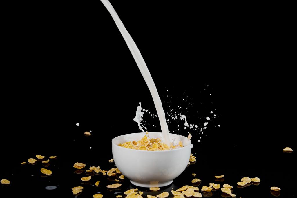 valkoinen kulho maissihiutaleet maitovirran ja roiskeet eristetty musta
 - Valokuva, kuva