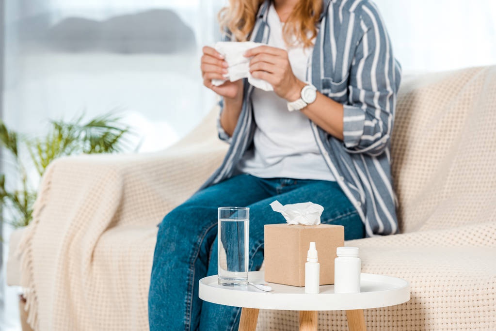 Ausgeschnittene Ansicht einer Frau, die auf einem Sofa sitzt und Serviette neben Glas mit Wasser hält  - Foto, Bild