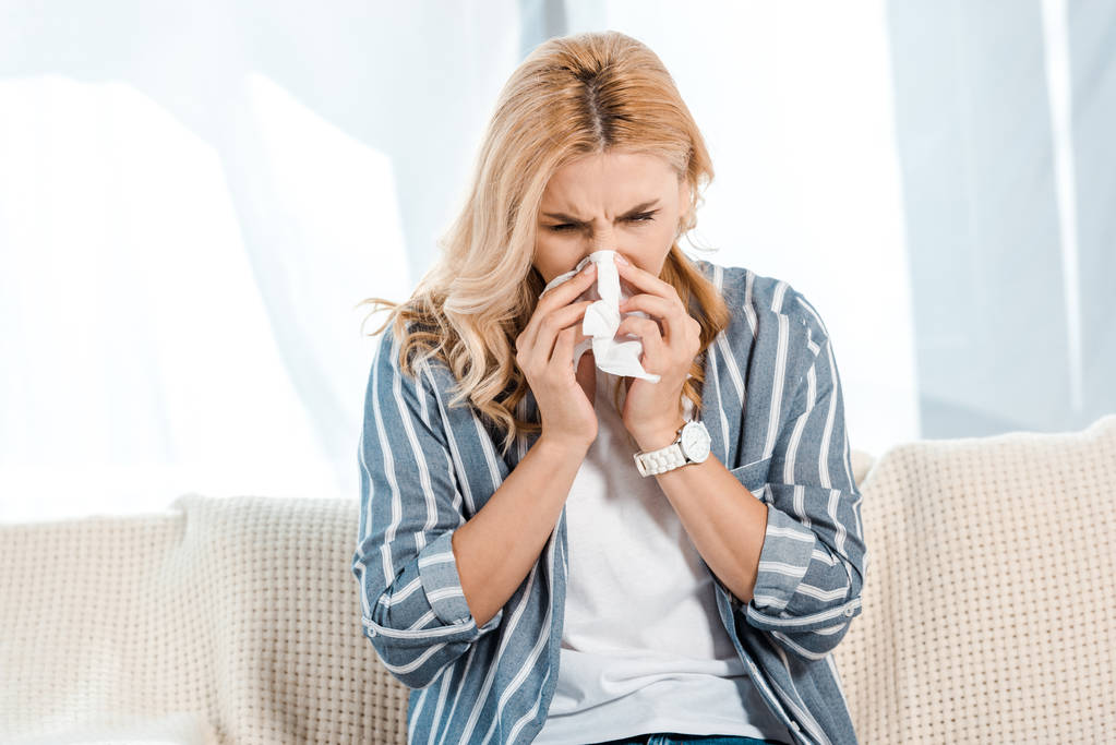 sick woman sitting on sofa and sneezing in napkin  - Photo, Image