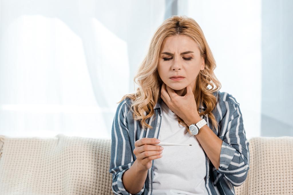 хвора жінка з болем в горлі і тримає електронний термометр
 - Фото, зображення