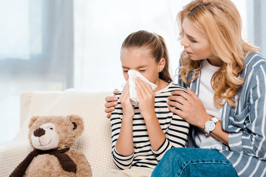 woman sitting near daughter sneezing in tissue near teddy bear  - Photo, Image
