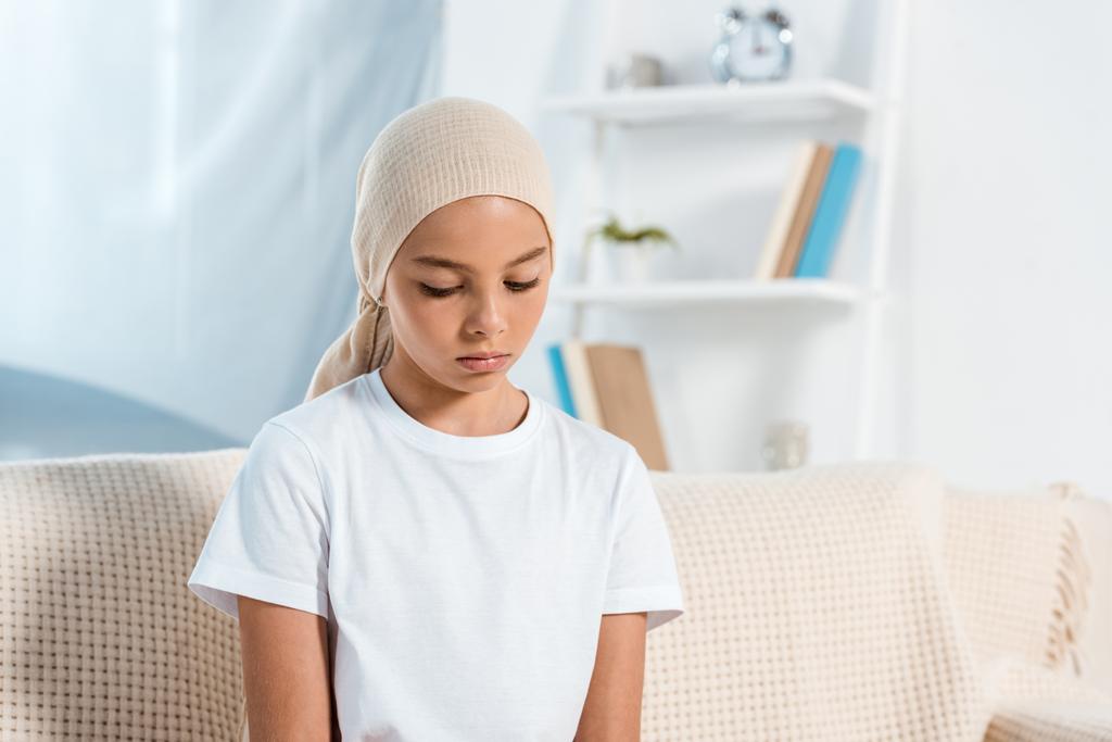 розчарована дитина в шарфі голови сидить на дивані у вітальні
  - Фото, зображення