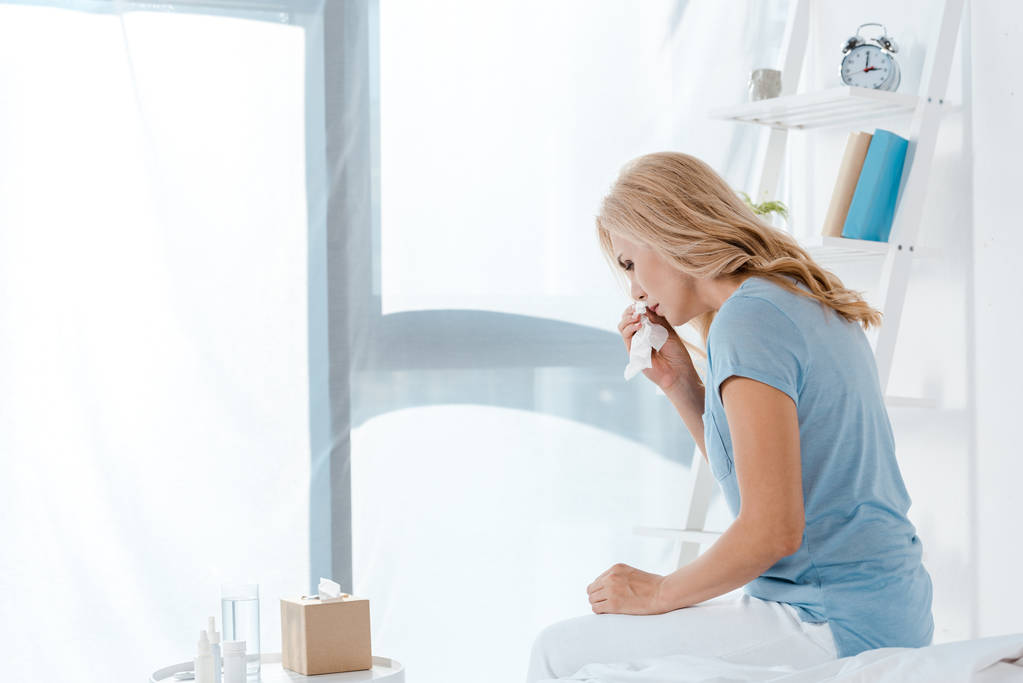 sick woman sitting on bed and holding napkin  - Photo, Image