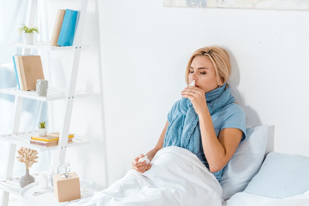chory kobieta trzymając aerozol do nosa w pobliżu nosa, leżąc w łóżku  - Zdjęcie, obraz