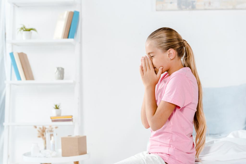 sick kid sneezing while sitting on bed in bedroom  - Photo, Image