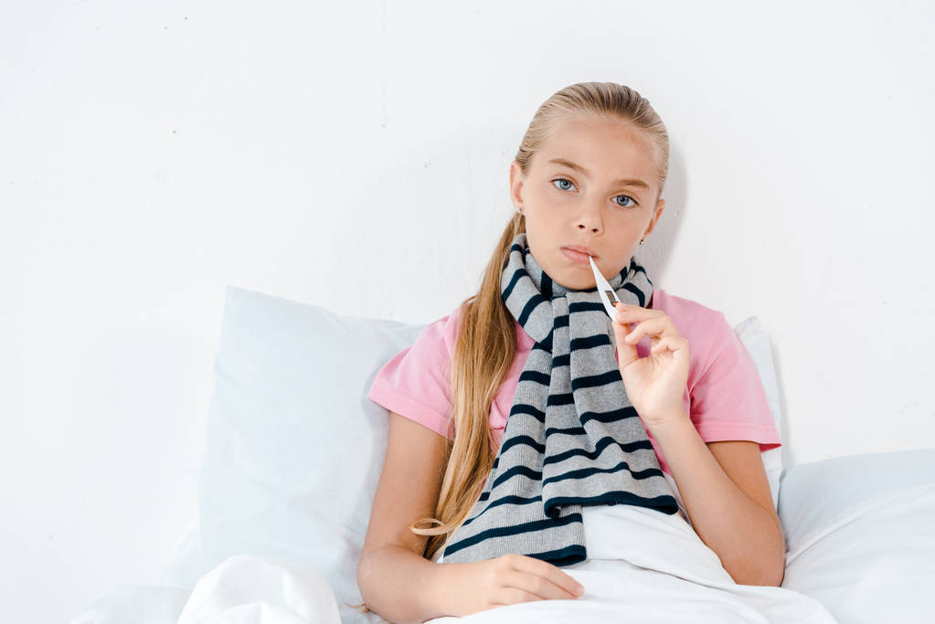 sick kid with digital thermometer in mouth looking at camera  - Photo, Image