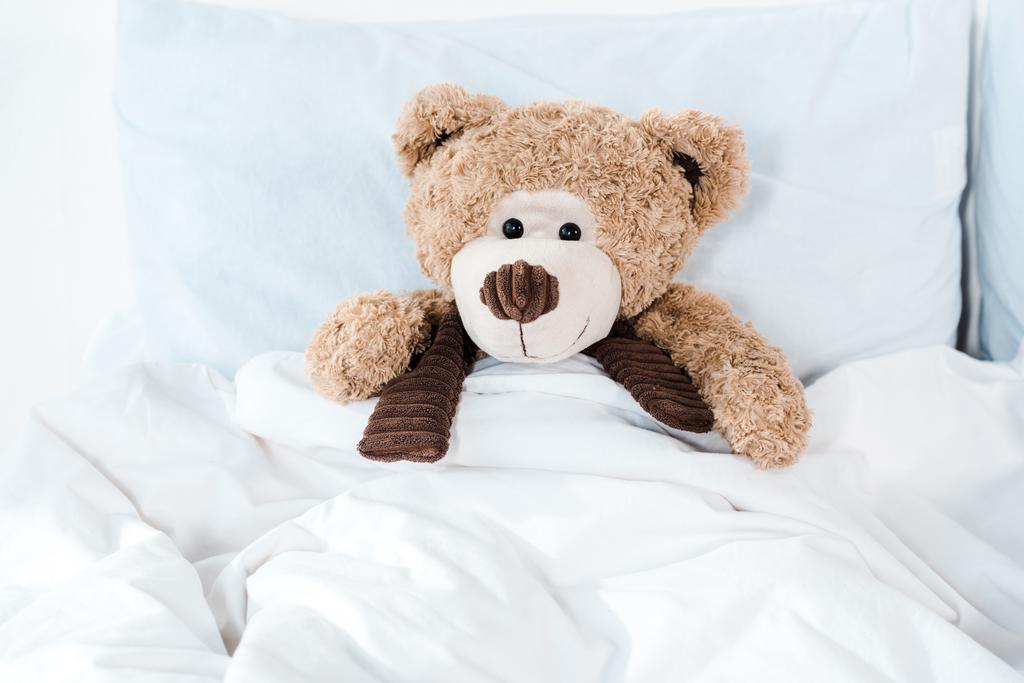 мягкая игрушка в постели с белыми постельными принадлежностями и подушками
  - Фото, изображение