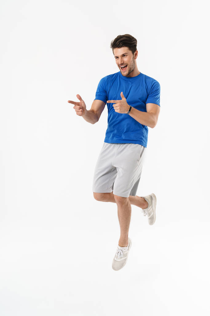 Handsome happy young sports fitness man standing isolated over white wall background make pointing with fingers gesture. - Photo, Image