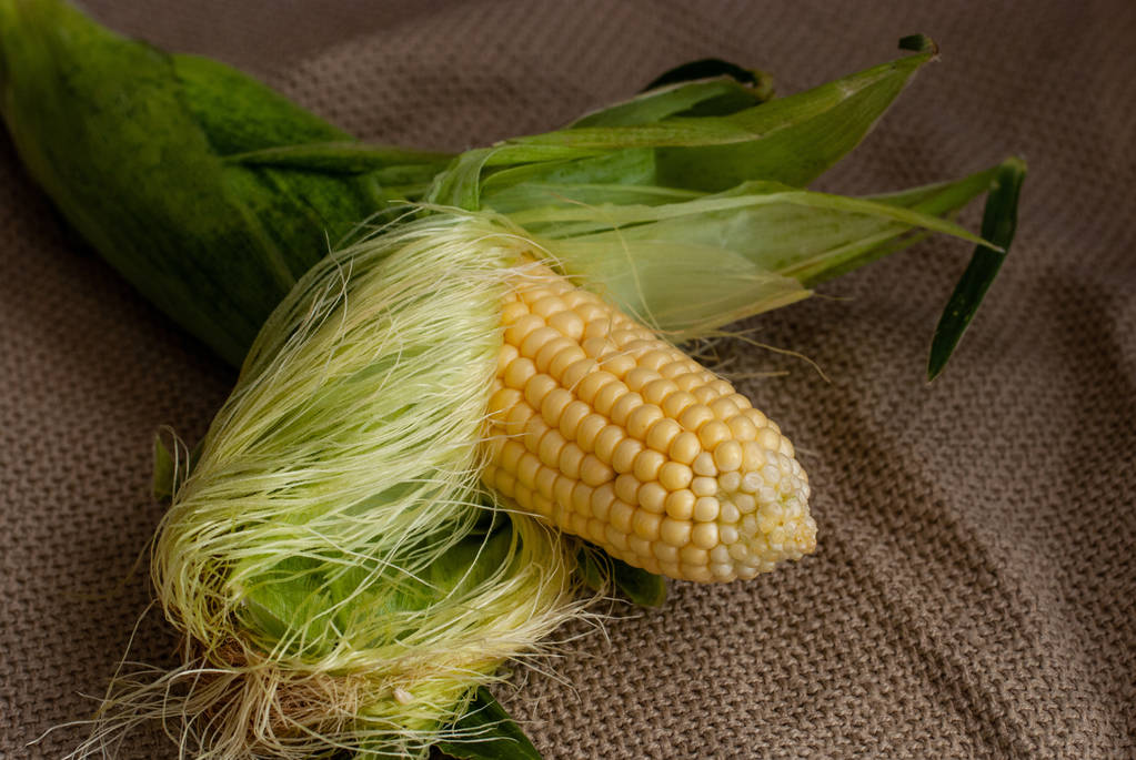 Il grano dolce crudo giallo è aperto da foglie verdi su un ba rustico
 - Foto, immagini