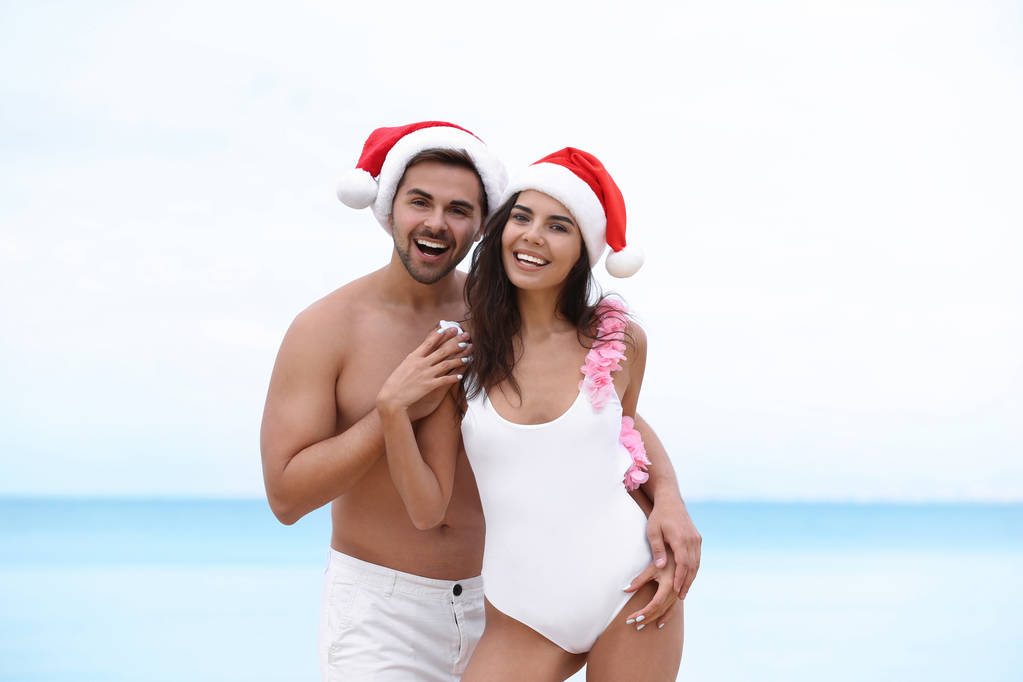 Šťastný mladý pár se Santa klobouky pohromadě na pláži - Fotografie, Obrázek